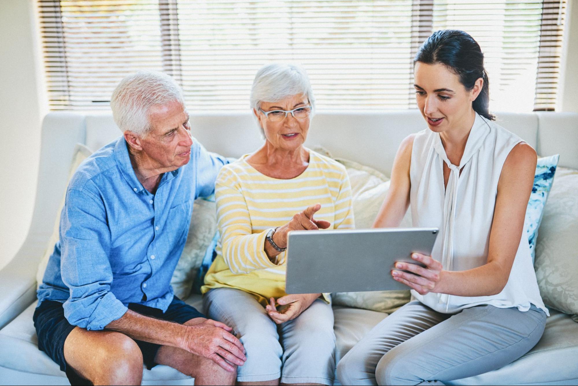 Senior care coordination meeting with an older couple reviewing options on a tablet
