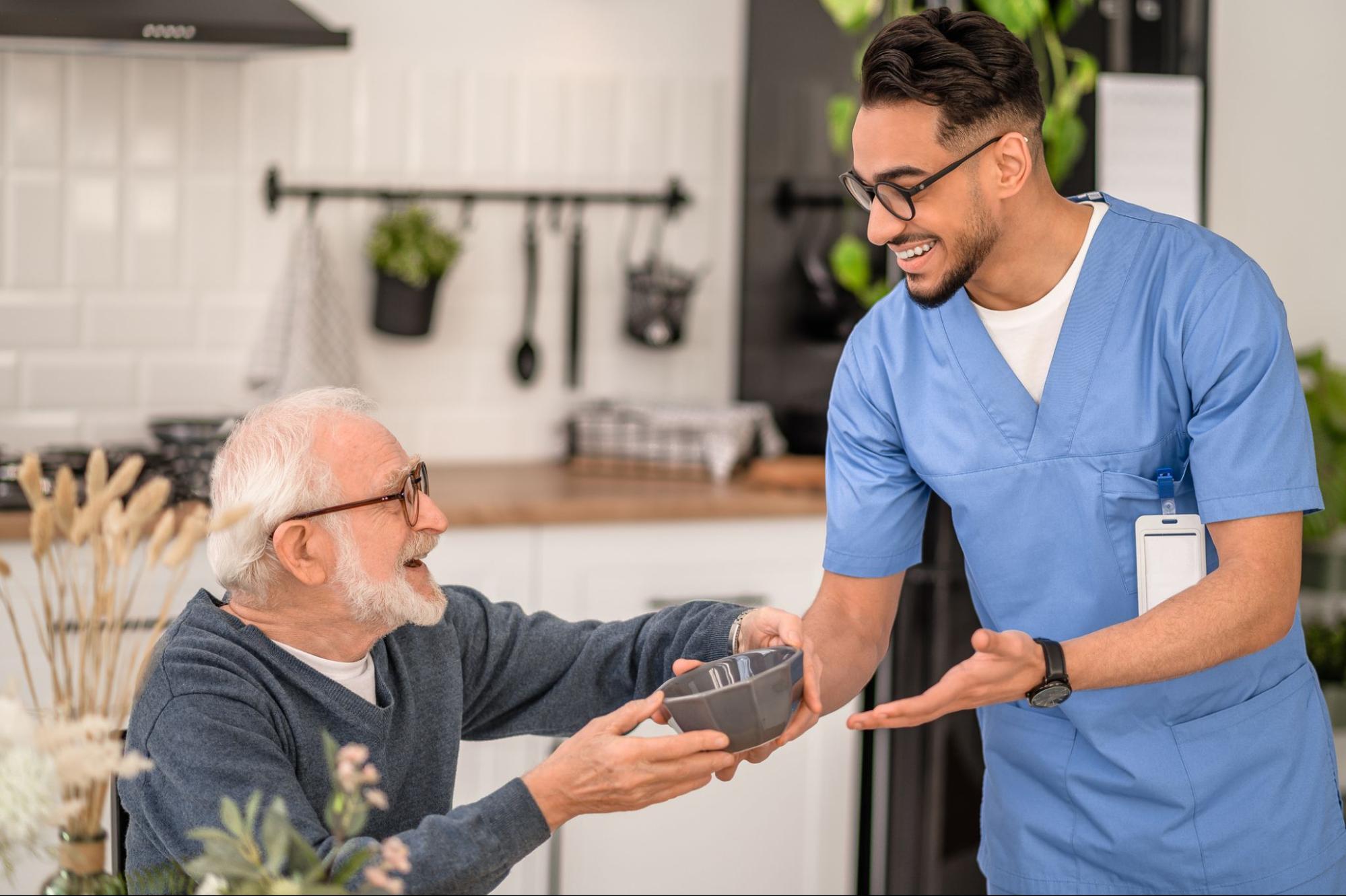 Caregiver serving a meal to a smiling older man during in-home companion care.