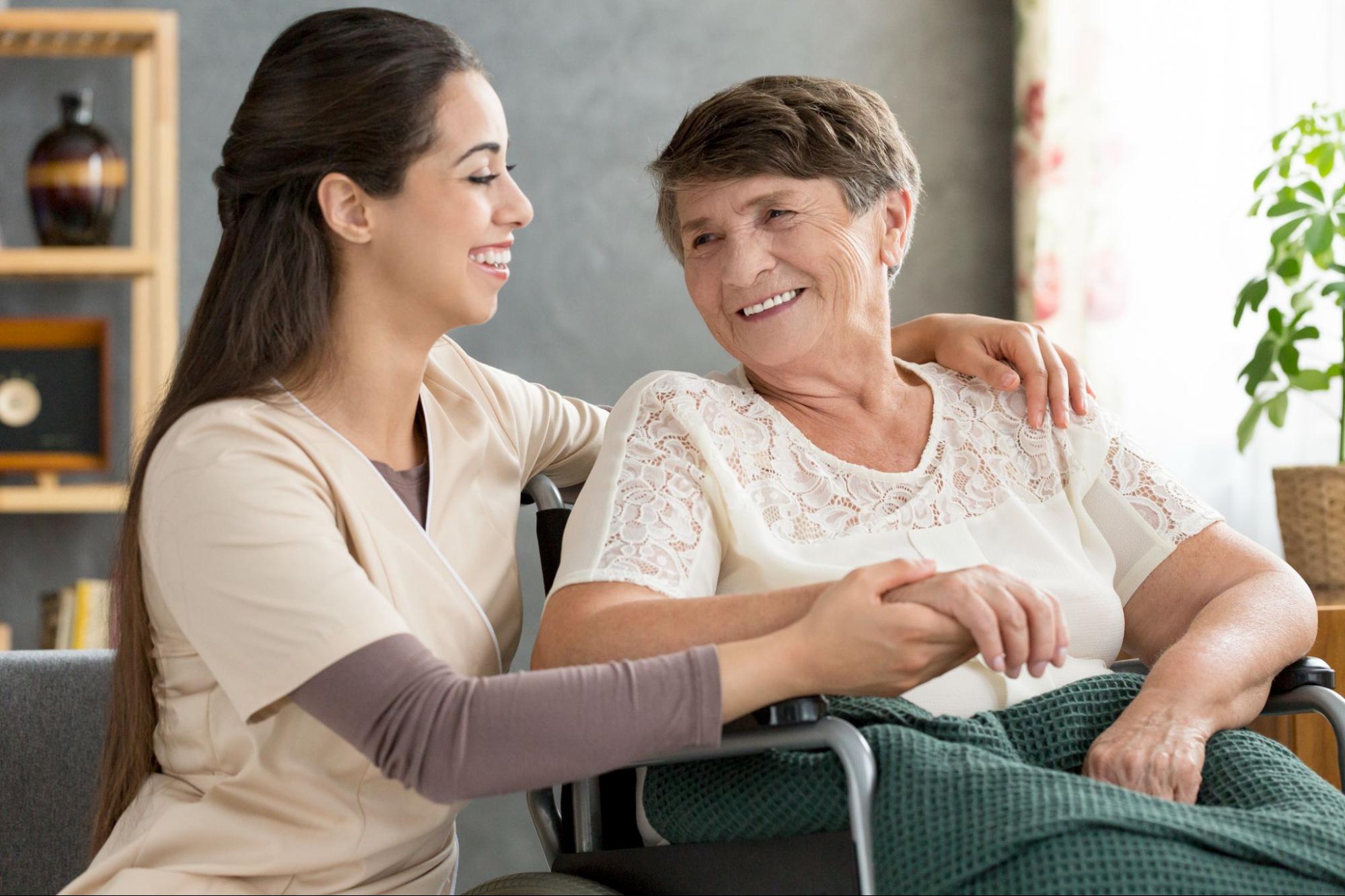 Smiling caregiver holds an older woman’s hand as part of toileting assistance for elderly.